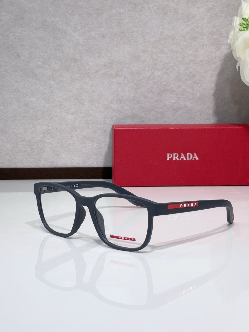 Dark blue eyeglasses with Prada mark on temple and red accent, rectangular frame.