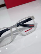 White eyeglasses close-up showing Prada logo and red accents on temple.
