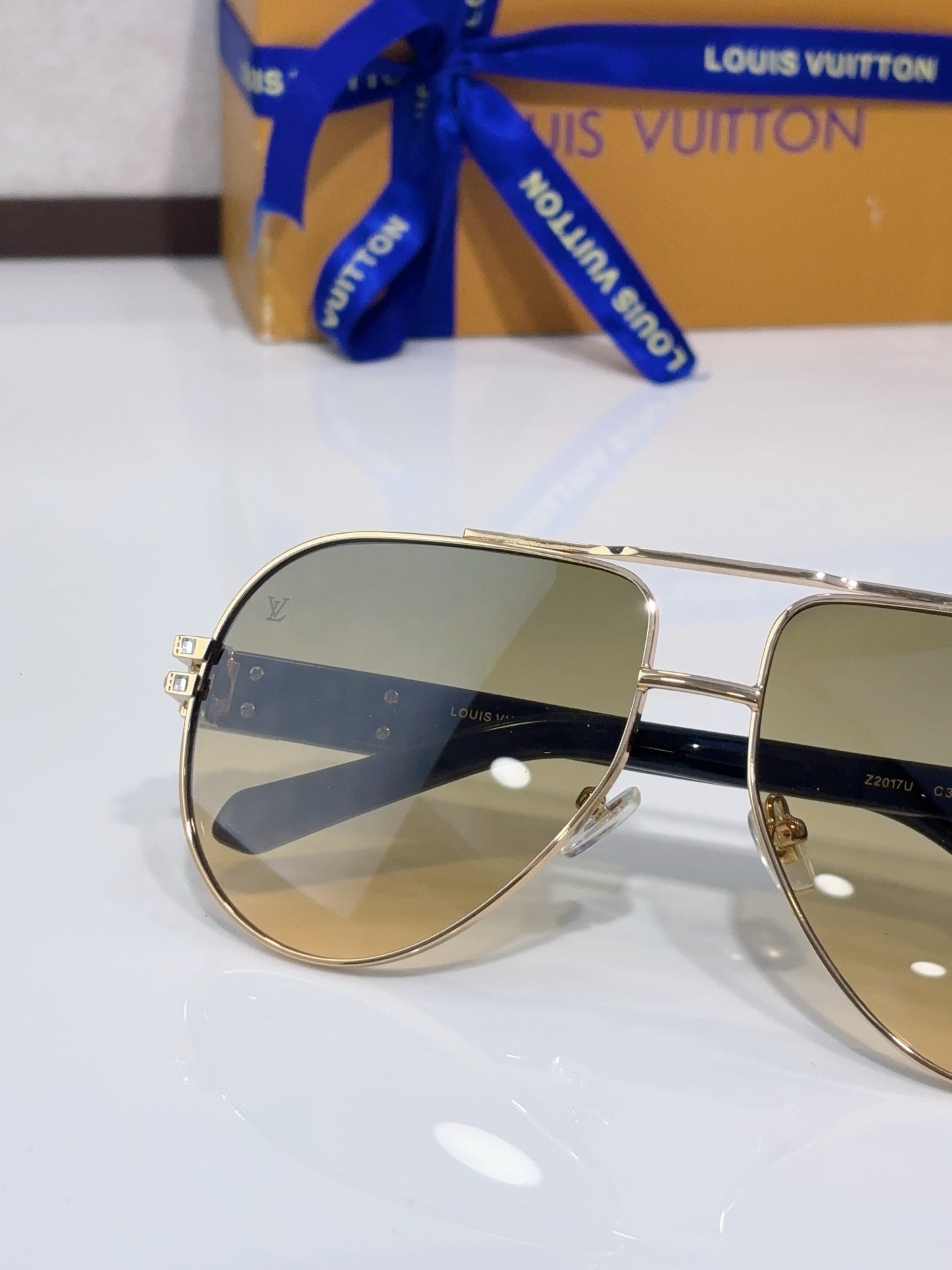 Close-up aviator sunglasses with tinted lenses and gold-tone metal frame, rhinestone detail.