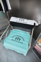 Turquoise T-shirt folded on display chair with rhinestone-style logo graphic
