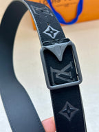 Black monogram belt buckle close-up with star motifs and gray finish