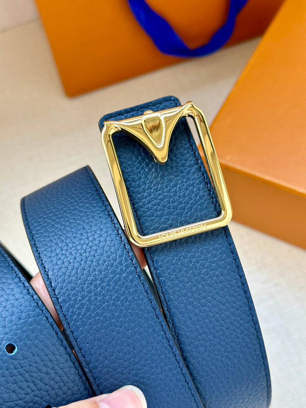 Louis Vuitton belt buckle close-up with gold-tone frame on blue leather strap