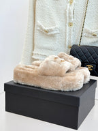 Beige faux fur slide sandals with gold-tone logo detail, on a box