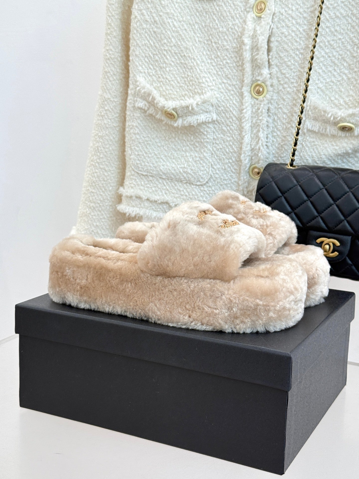 Beige faux fur slide sandals with gold-tone logo detail, on a box