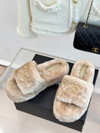 Pair of beige faux fur slide sandals with gold logo on straps