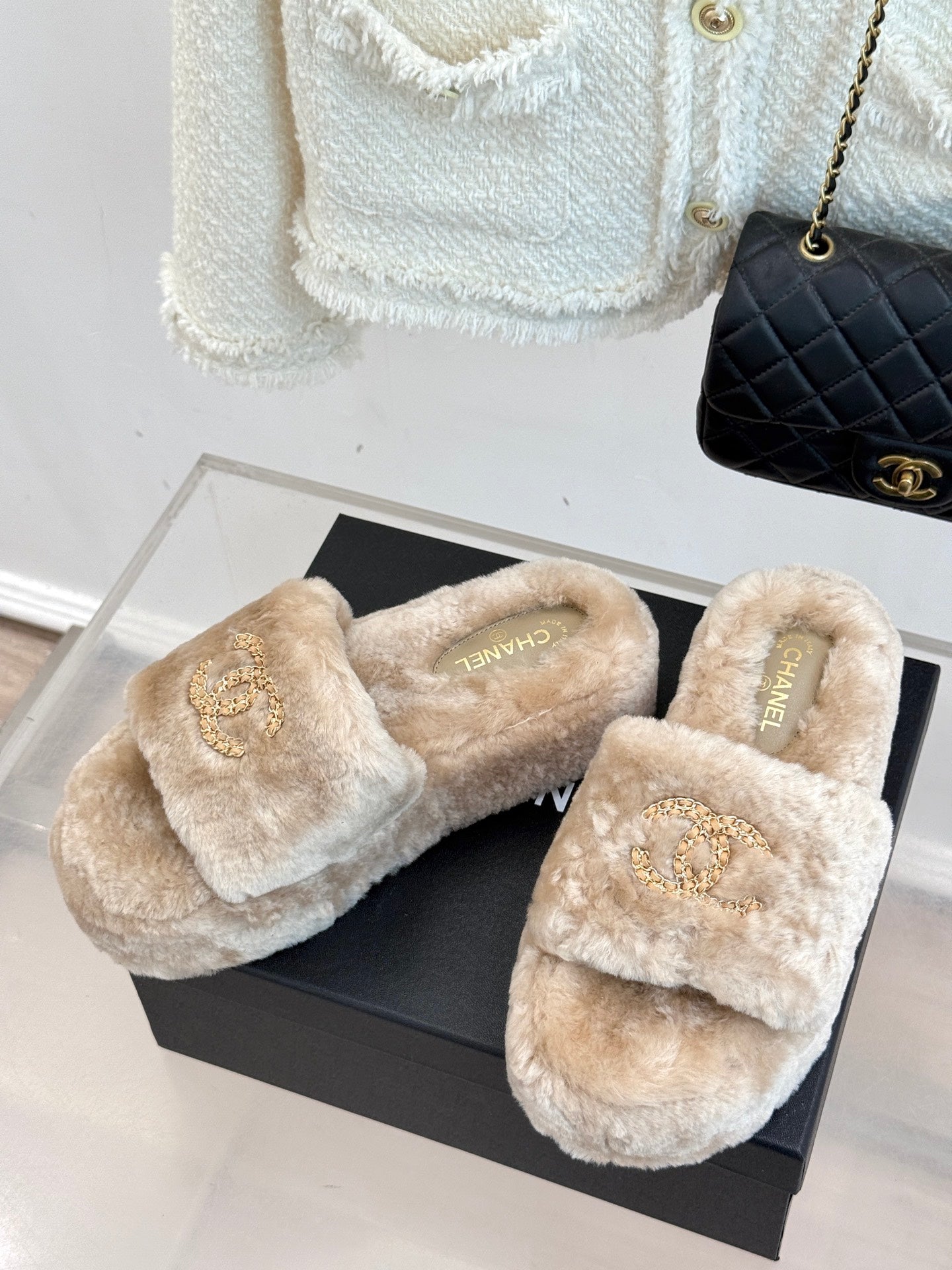 Pair of beige faux fur slide sandals with gold logo on straps