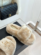 Beige faux fur slide sandals with gold logo detail, shown on display box