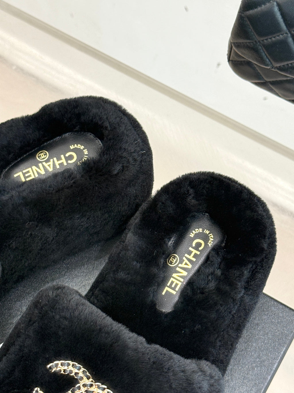 Black faux-fur CHANEL slides with gold logo lettering on the footbed