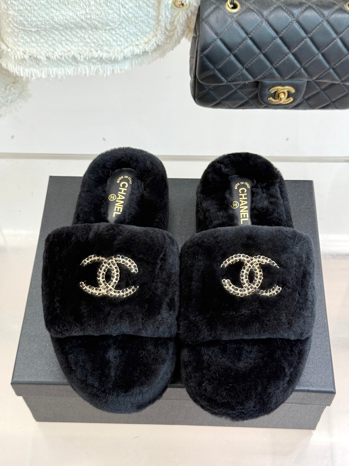 Black fuzzy slide sandals featuring a gold-tone CHANEL logo on the front