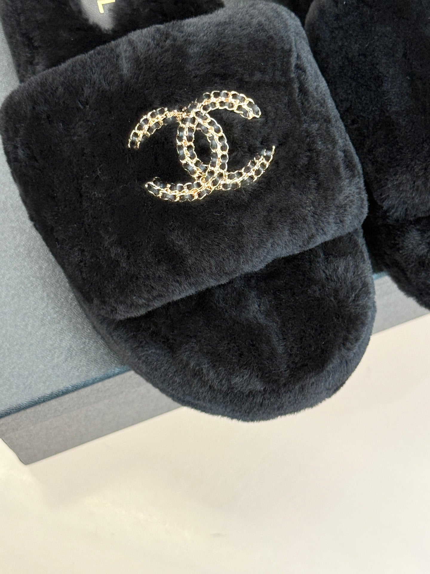Close-up of black faux-fur CHANEL slide sandal with gold-tone logo on the strap