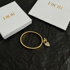 Gold-tone open cuff bracelet with small floral charm and pavé heart drop