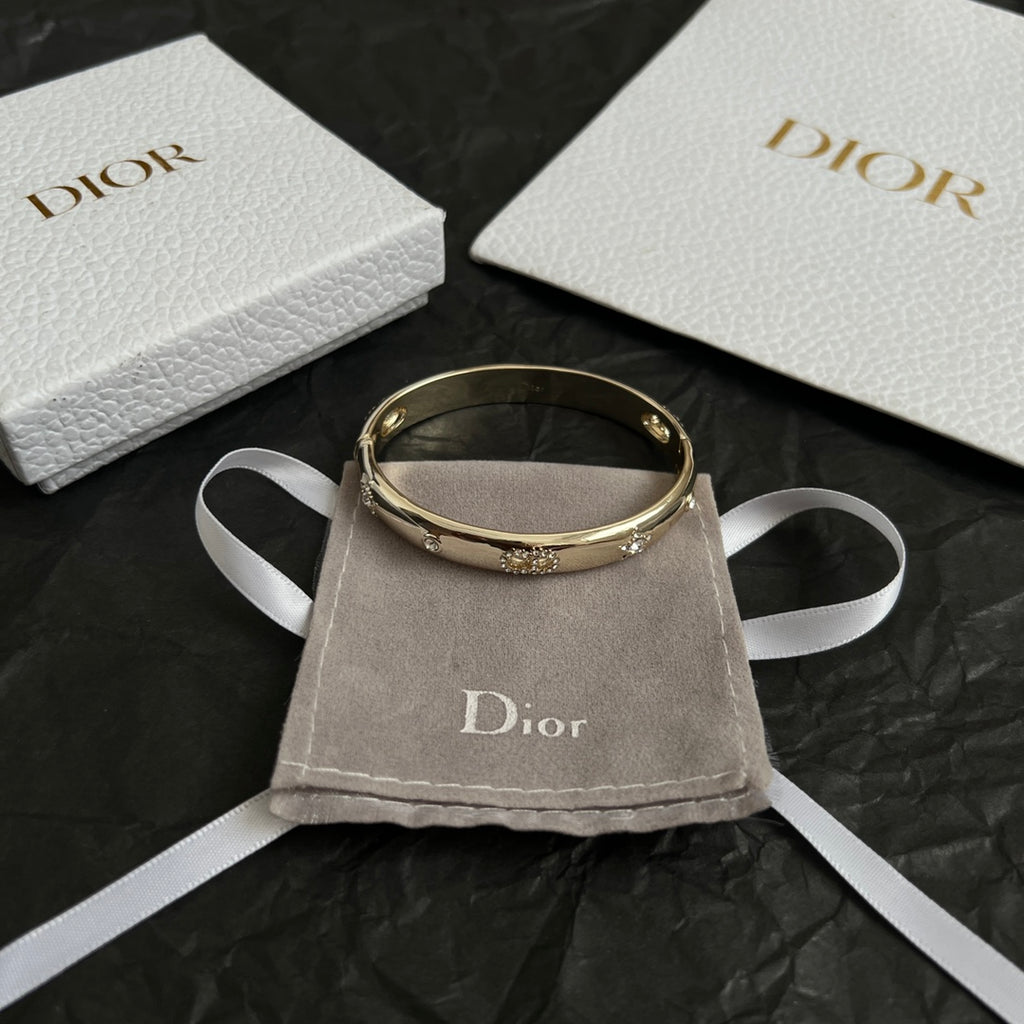 Gold-tone Dior bangle bracelet with small clear stones, shown on a pouch.