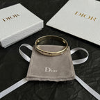 Gold-tone Dior bangle bracelet with small clear stones, shown on a pouch.