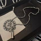 Beaded metal necklace with cylindrical pendant, shown with fabric pouch and box