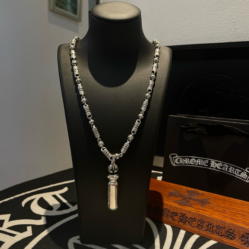 Beaded metal necklace on display bust, with tall cylindrical pendant