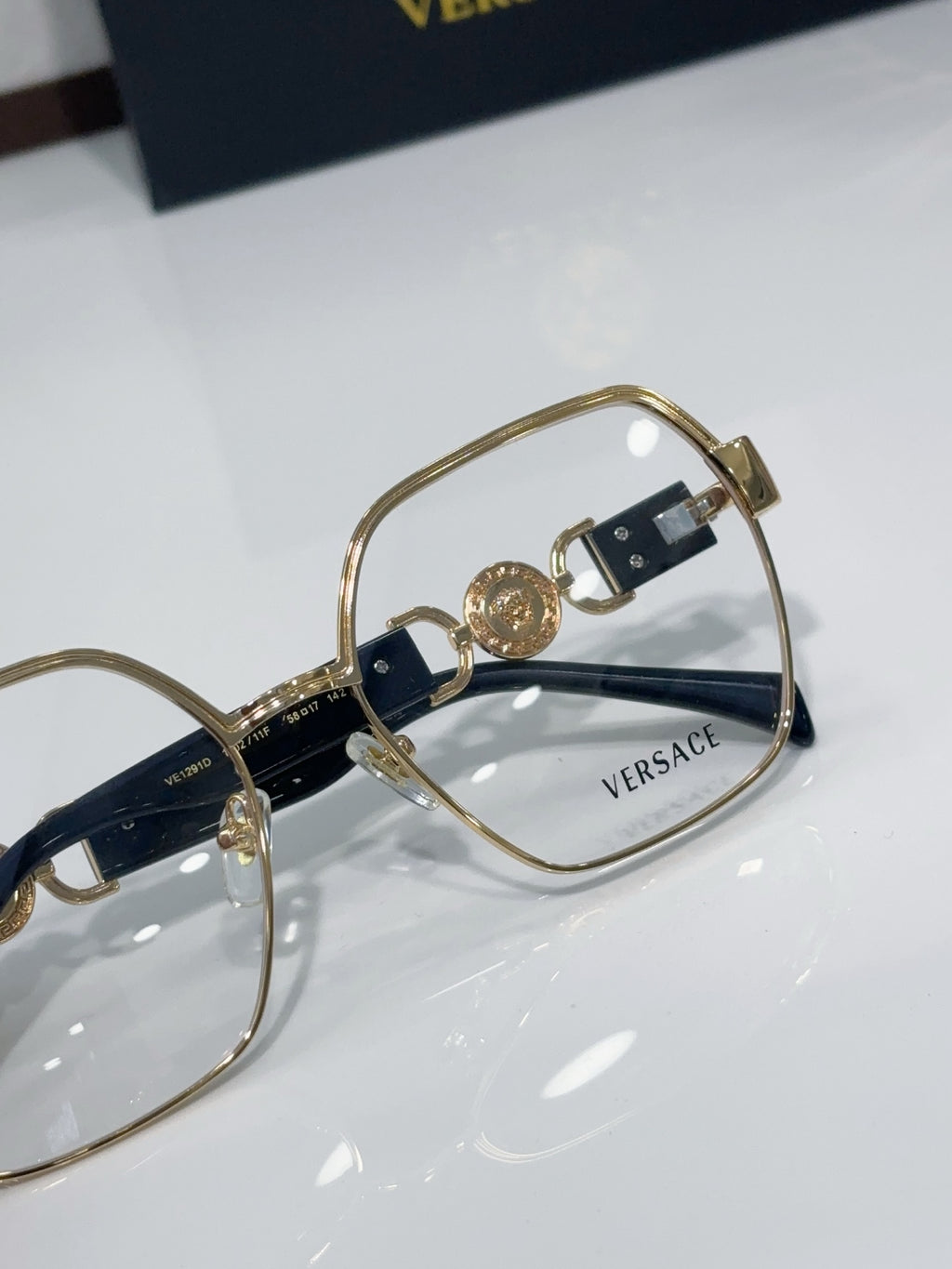 Versace eyeglasses close-up: gold-tone frame with navy temple accents and logo plaques