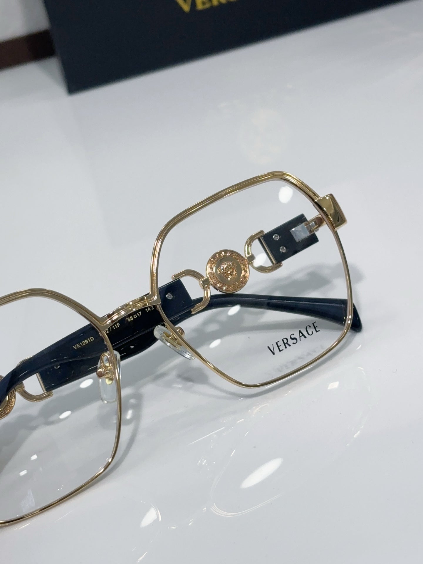 Versace eyeglasses close-up: gold-tone frame with navy temple accents and logo plaques