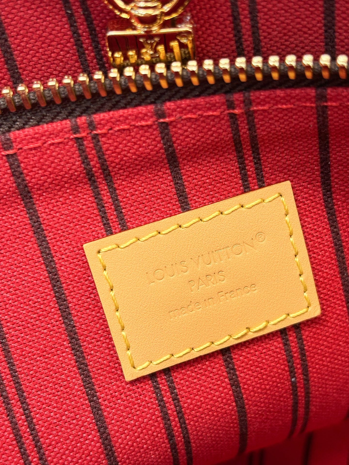 Louis Vuitton monogram pouch label on red-and-black striped fabric with stitching
