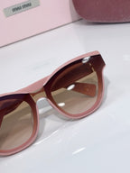 MiuMiu cat-eye sunglasses close-up, pale pink frame with brown tinted lens