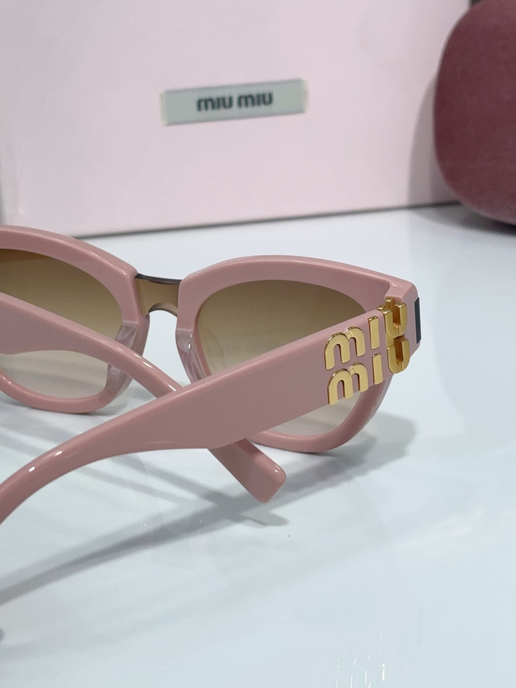 MiuMiu cat-eye sunglasses close-up, pale pink frame with gold side logo