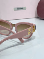 MiuMiu cat-eye sunglasses close-up, pale pink frame with gold side logo