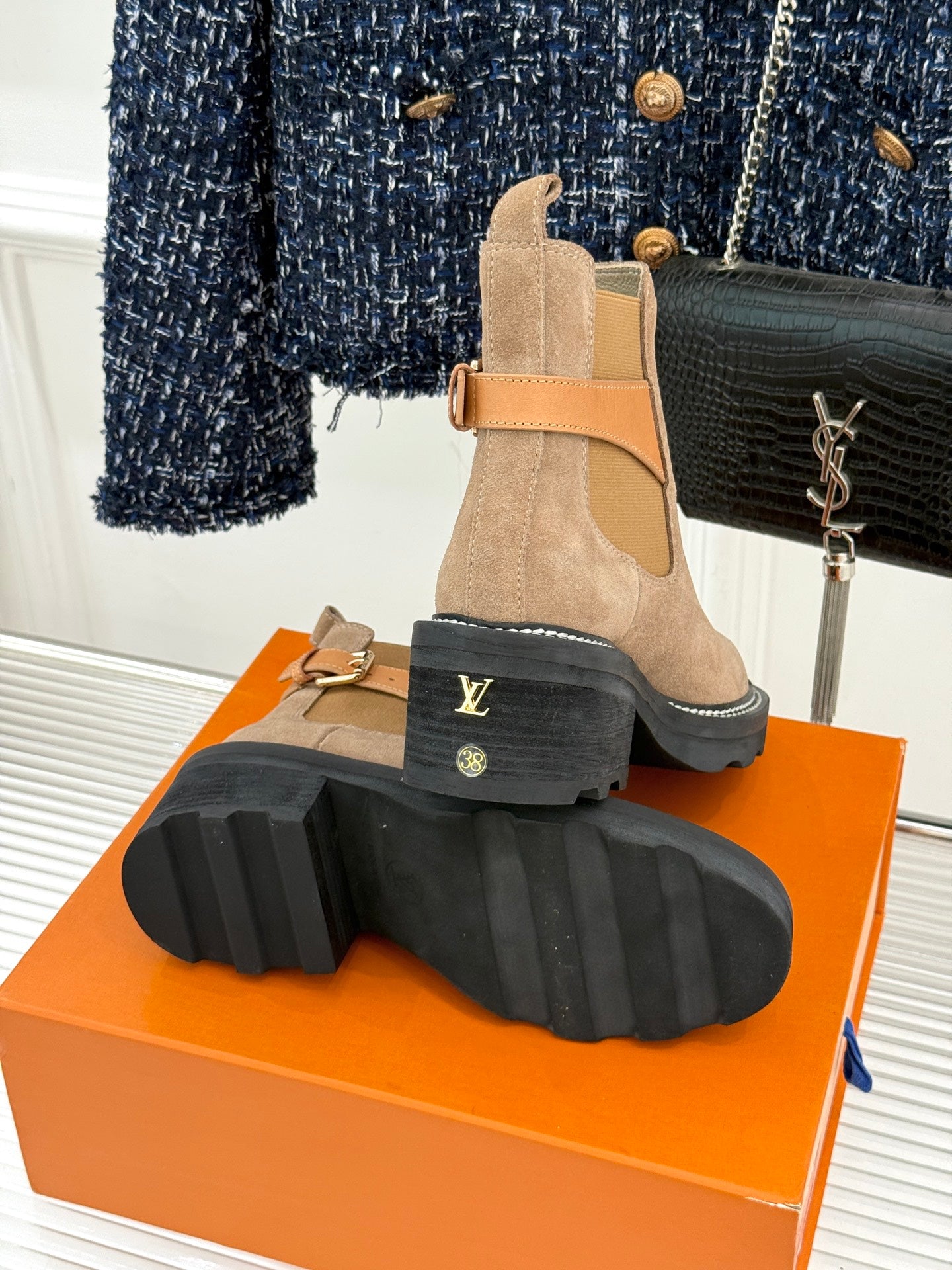 Beige suede ankle boot showing tread sole, buckle strap, and side elastic panels