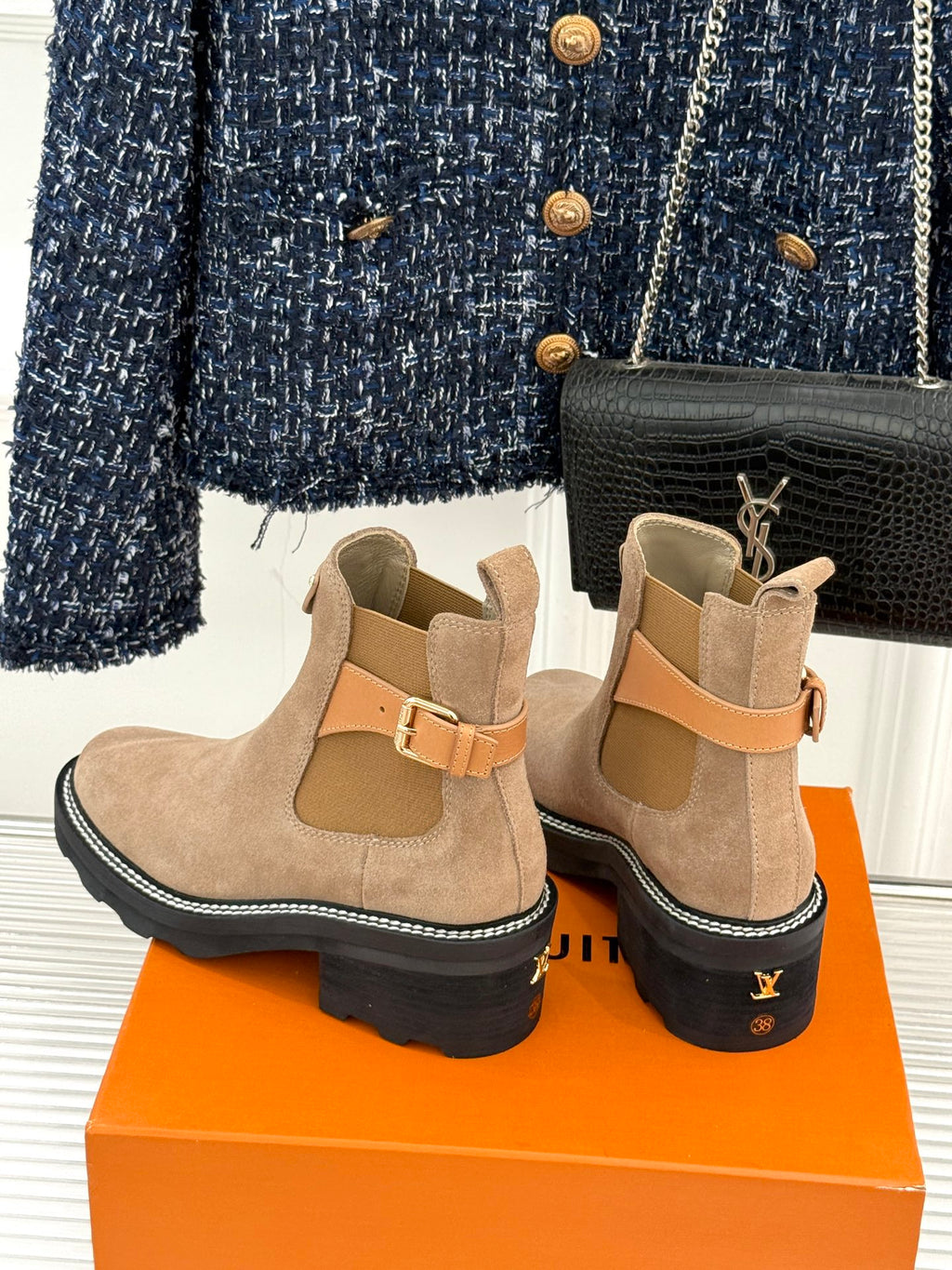 Beige suede ankle boots with buckle strap and black topstitching around sole