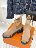 Pair of beige suede ankle boots with buckle strap and dark rubber sole