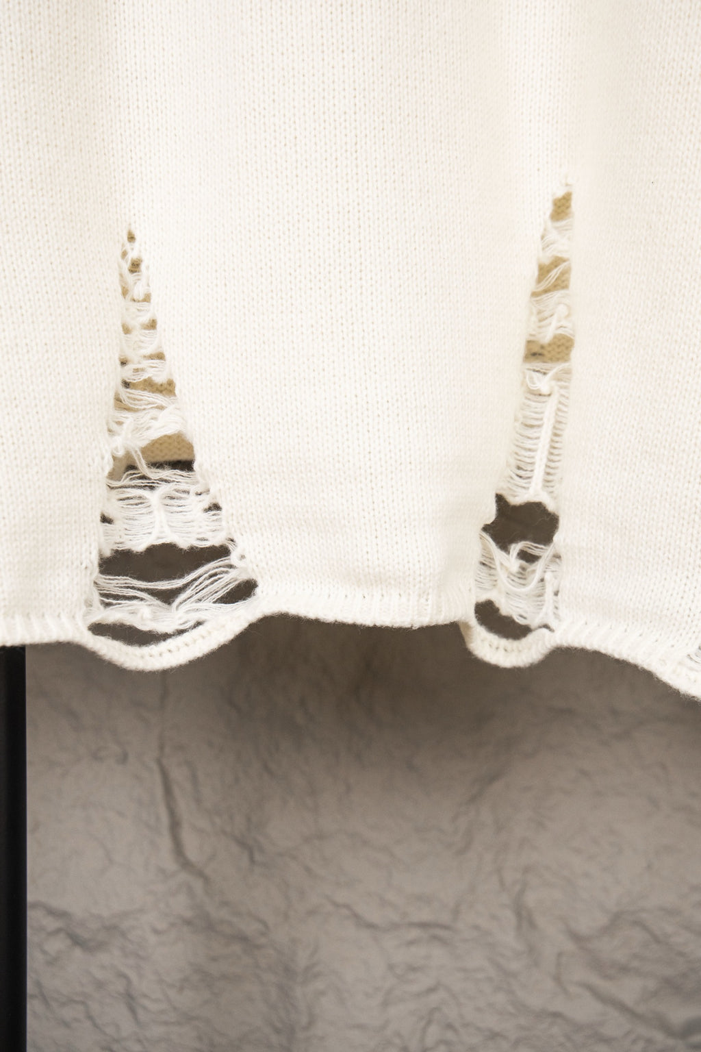 White knit sweater hem with frayed sleeves and cutout stitching