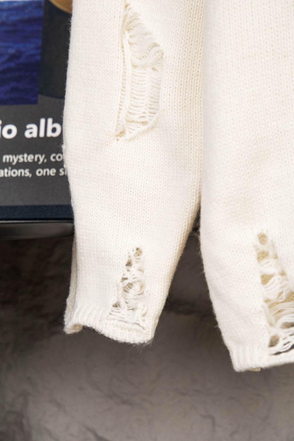 White knit sweater sleeve hem with frayed cutout detail