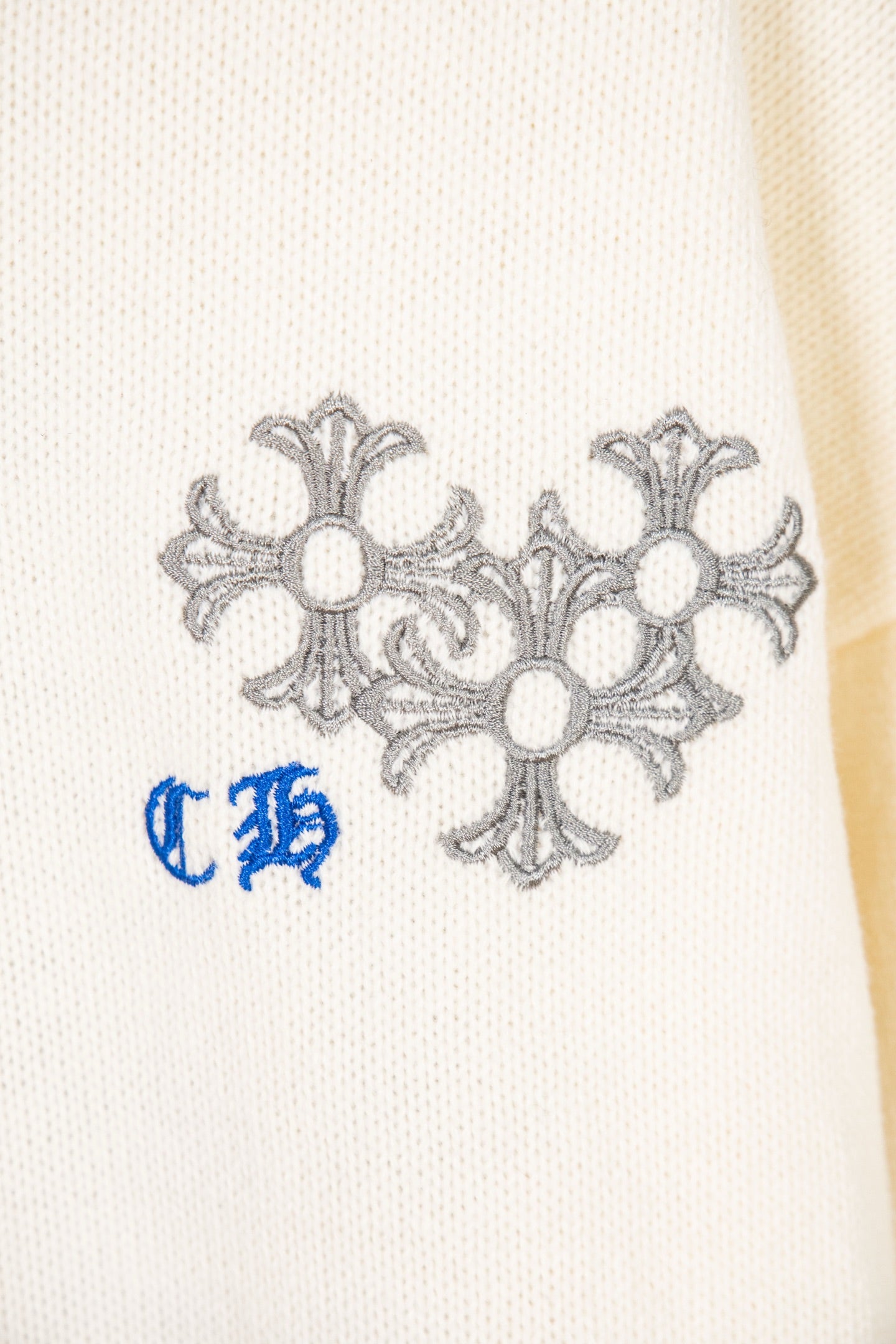 White knit sweater sleeve with gray flower motif and blue stylized letters
