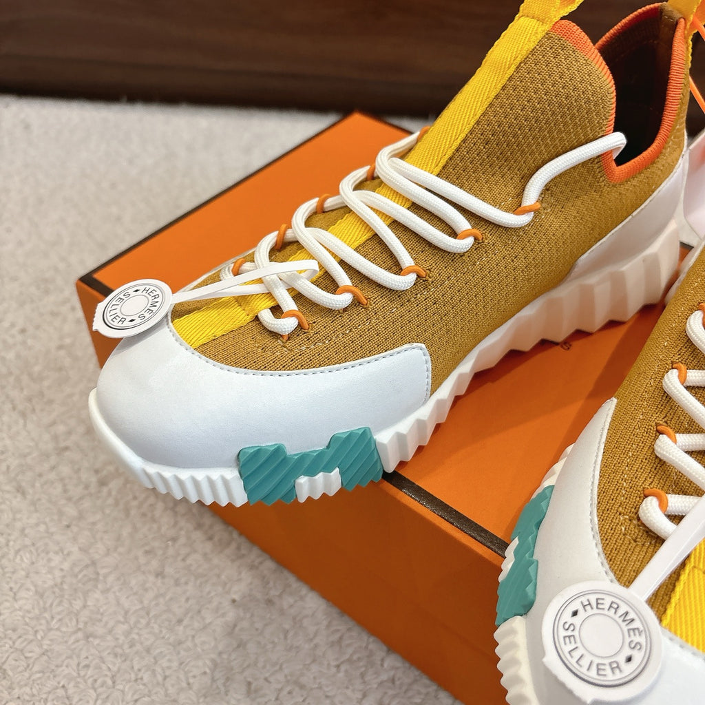 Hermes unisex sneakers close-up, knit brown upper, white laces, teal ridged outsole.
