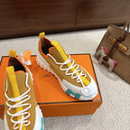 Hermes unisex sneakers on box, white laces, teal outsole detail, orange/red heel lining.