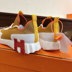 Hermes unisex sneakers heel view, brown upper with red and orange inserts, thick white sole.