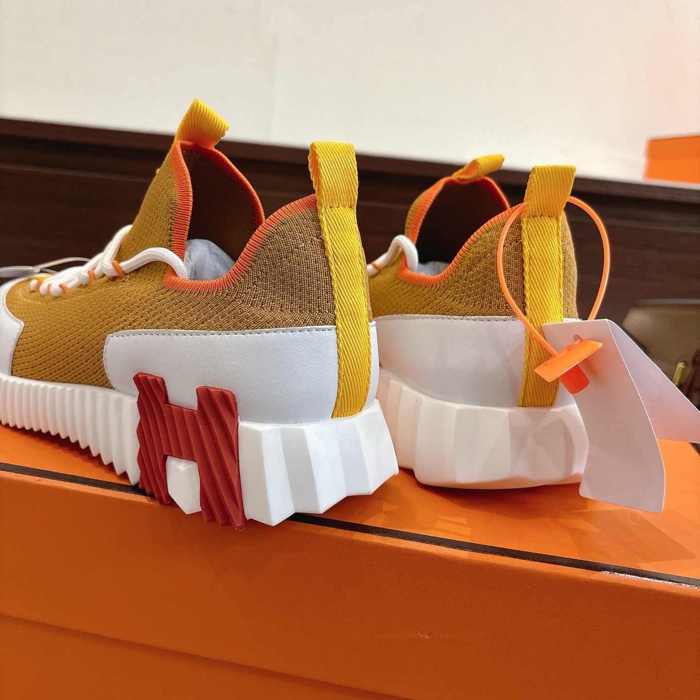Hermes unisex sneakers heel view, brown upper with red and orange inserts, thick white sole.