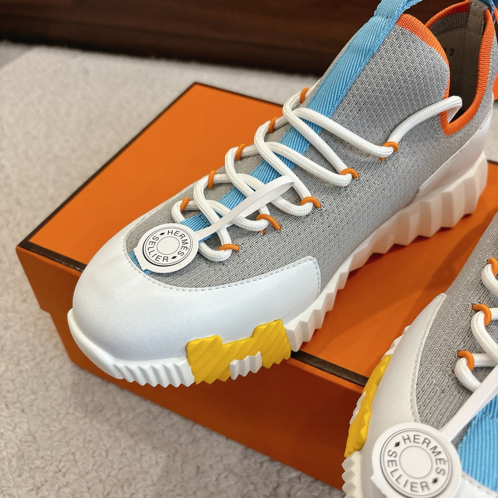 Close-up of unisex luxury sneaker: grey upper, blue lace loops, white laces, chunky sole