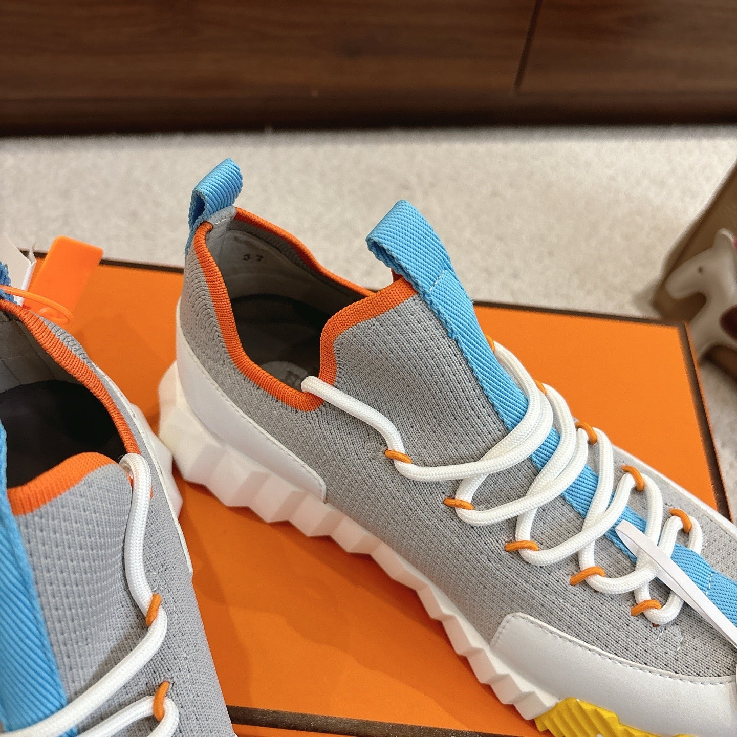 Side view of unisex luxury sneakers: grey knit upper, blue elastic straps, white laces