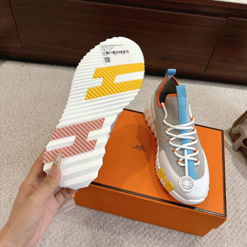 Unisex luxury sneaker outsole with chunky tread in white and colored accents, on orange box