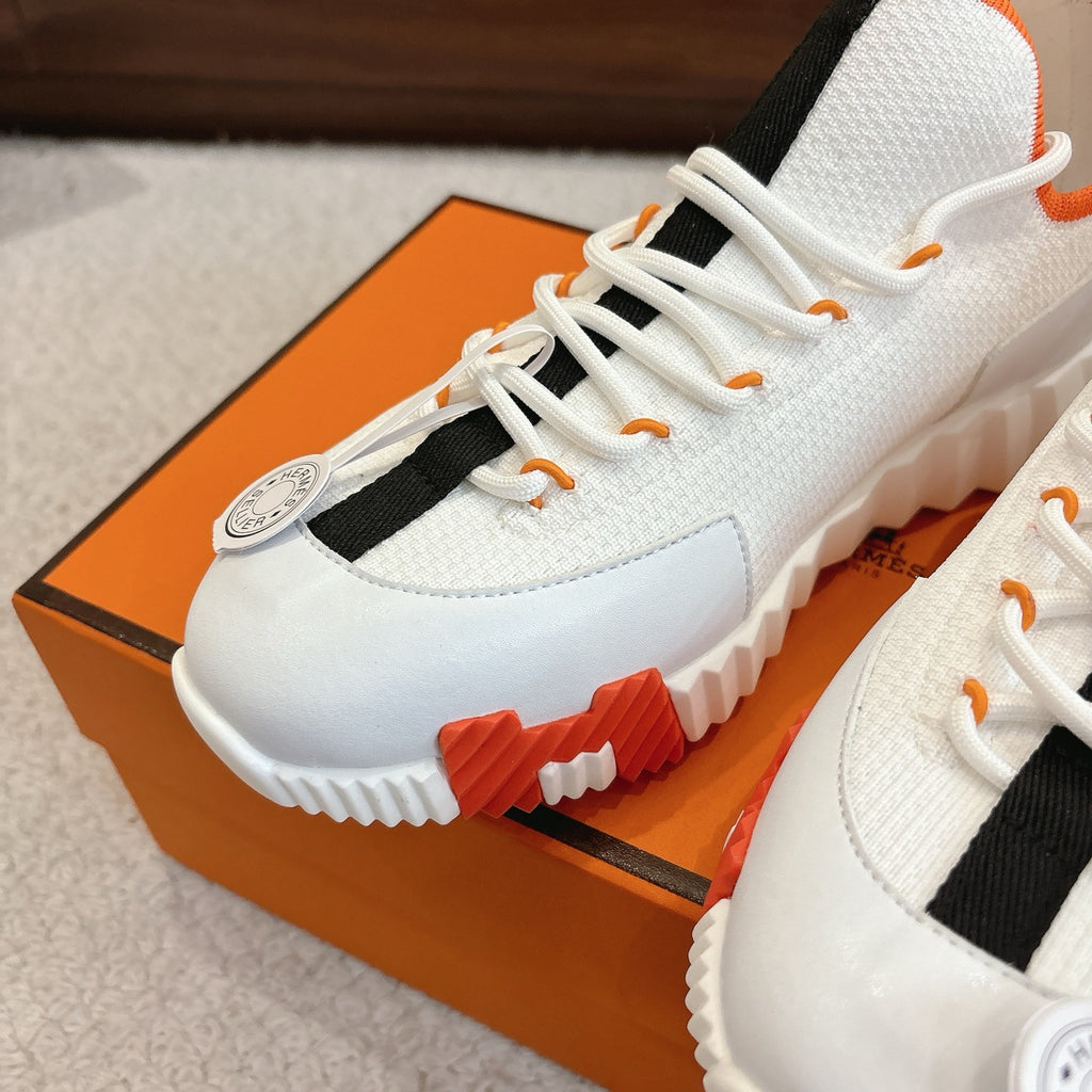 White sneaker toe cap with orange lace tips, black side strap, tread outsole