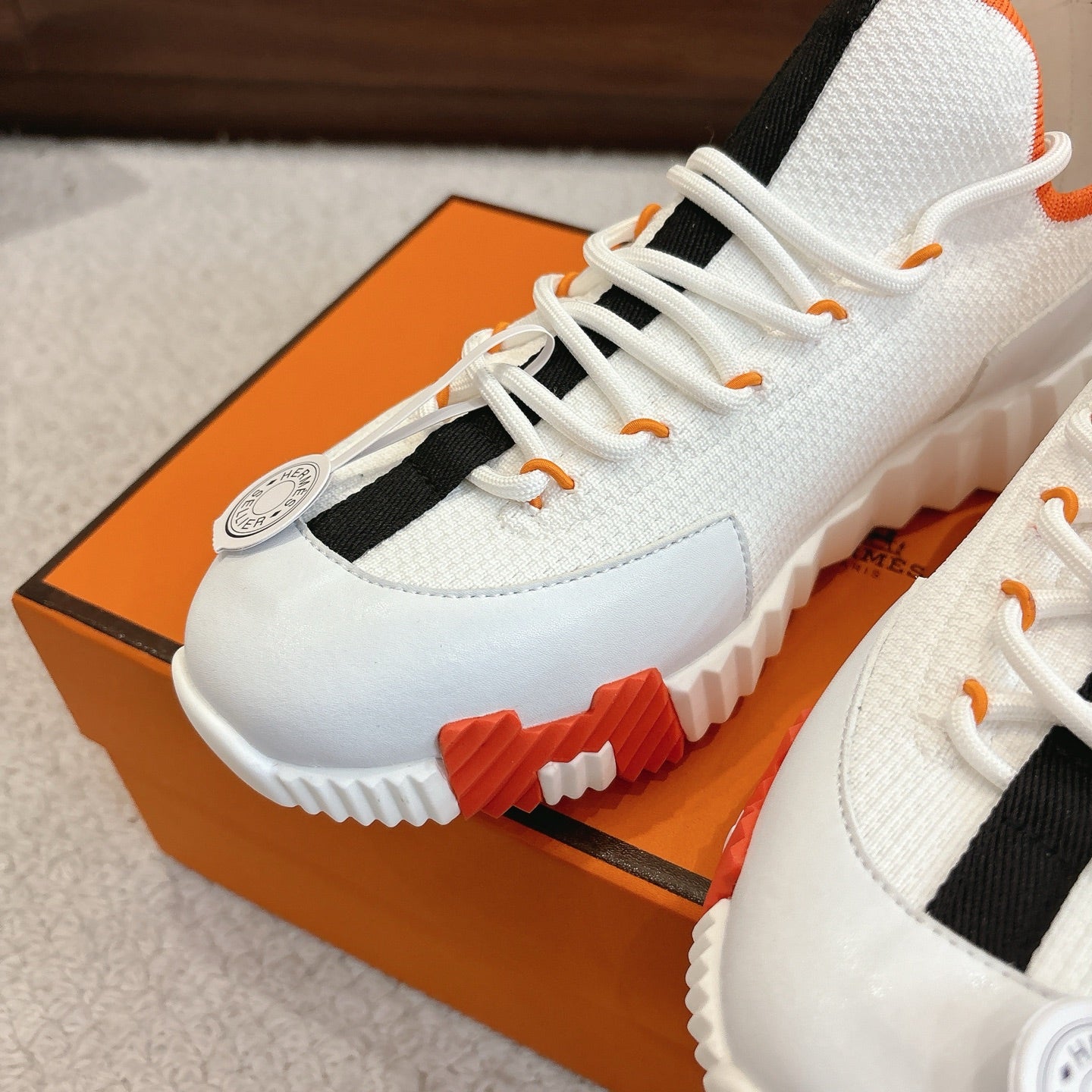 White sneaker toe cap with orange lace tips, black side strap, tread outsole