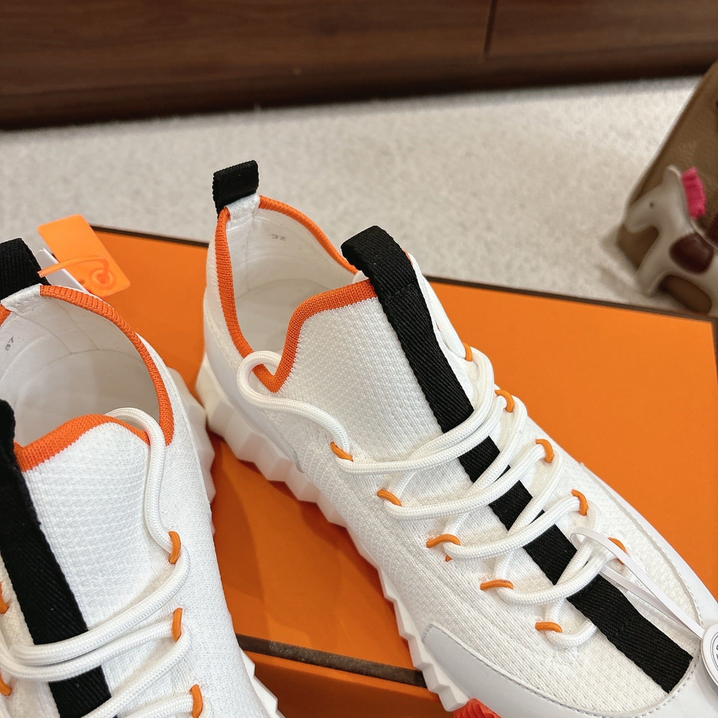 White sneakers close-up with black ankle straps, orange piping, lace-up front