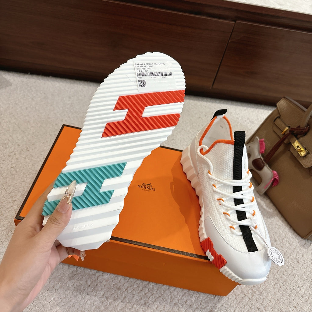 White sneakers outsole view with orange-striped tread and teal side details