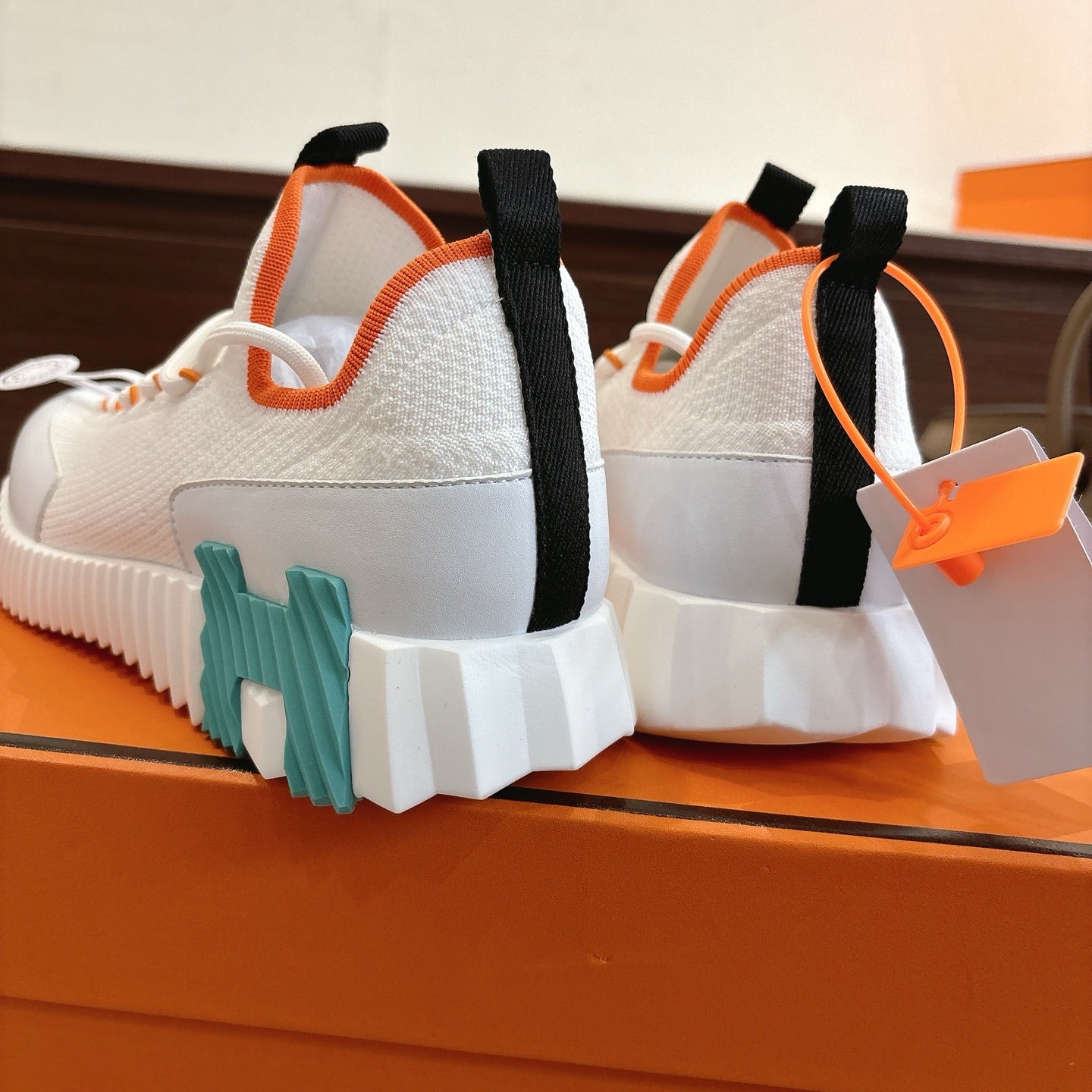 White sneakers rear view with black heel straps, orange trim, and teal sole inserts