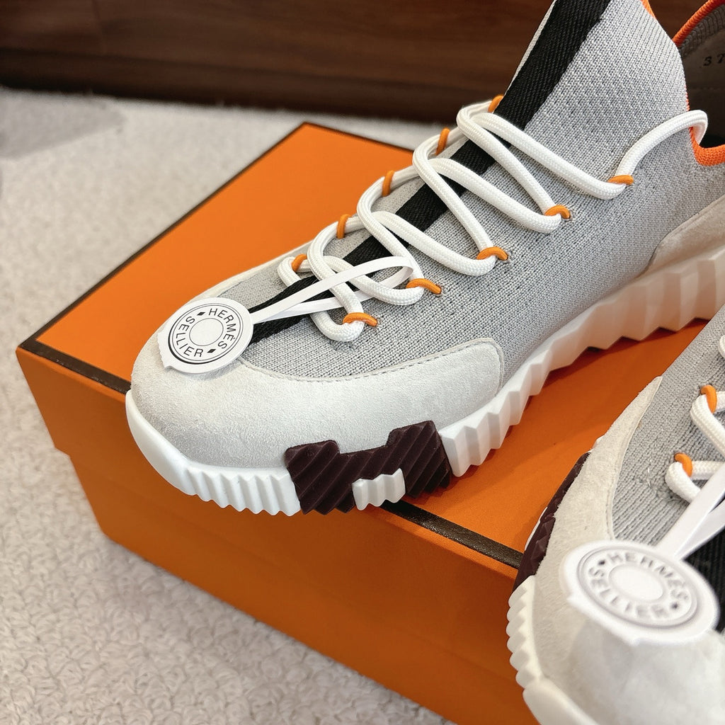 Gray sneaker detail: white laces, round logo patch, black accent, white tread sole