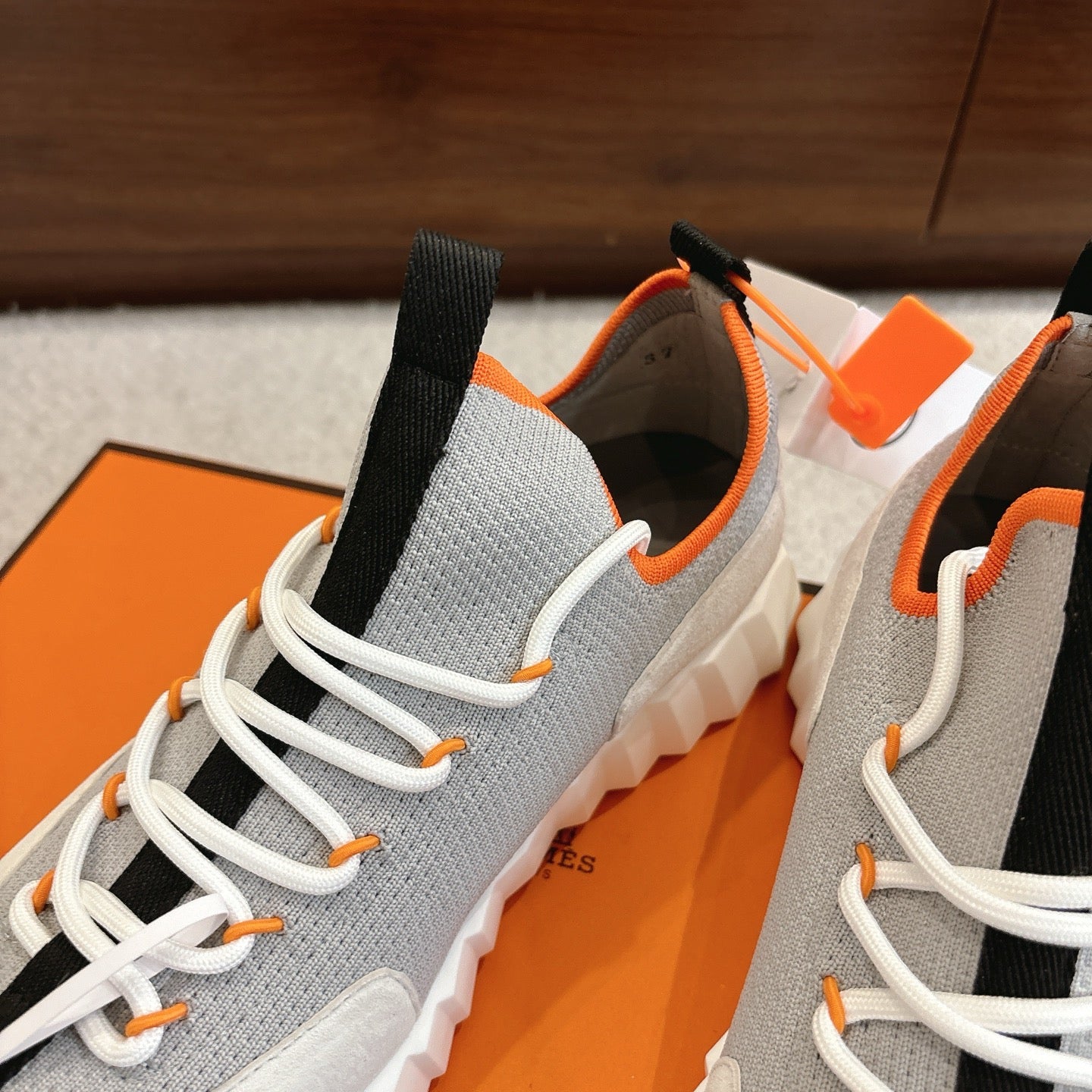 Gray sneaker close-up with white laces, black collar tab, orange edging, cushioned sole