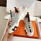 Gray lace-up sneaker pair in orange box, white laces, black panels, orange lining, tread sole