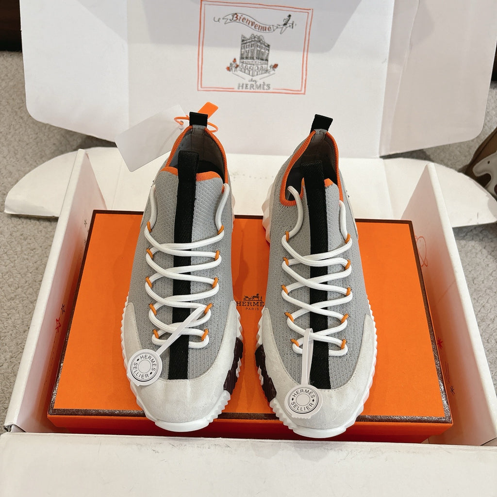 Gray knit sneaker with white laces, black side panels, orange trim, chunky white sole