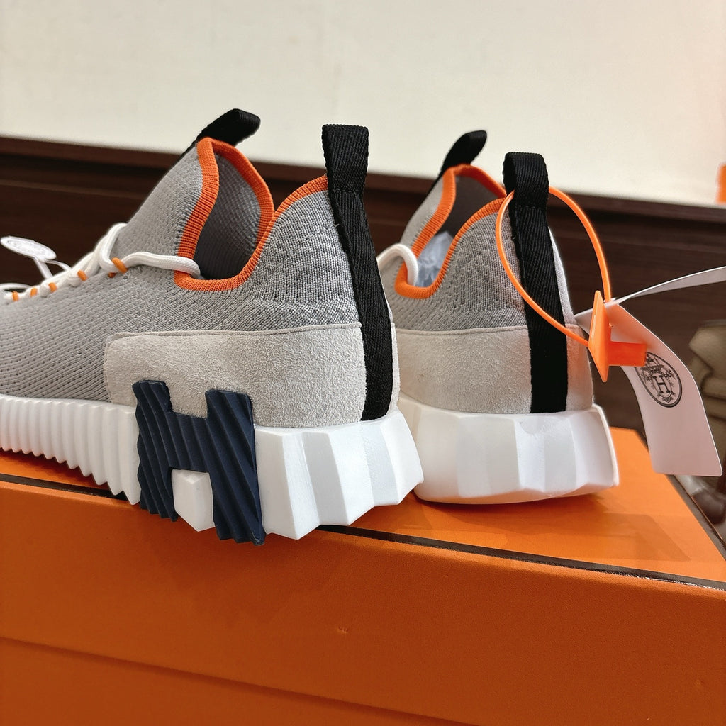 Gray sneakers viewed from heel, white outsole tread, black heel tabs, orange lining trim