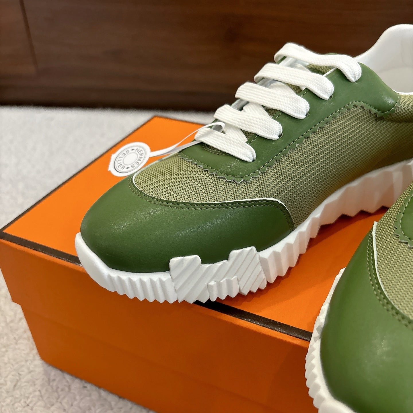 Close-up: green Hermes unisex sneaker with white laces and curved leather toe
