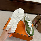Green Hermes unisex sneakers showing white treaded outsole on orange box
